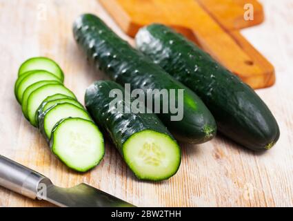 Primo piano di cetrioli freschi con fette tagliate su superficie di legno. Cibo vegetariano Foto Stock