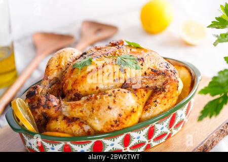 Pollo arrosto intero con prezzemolo fresco e spicchi di limone in un piatto di festa Foto Stock