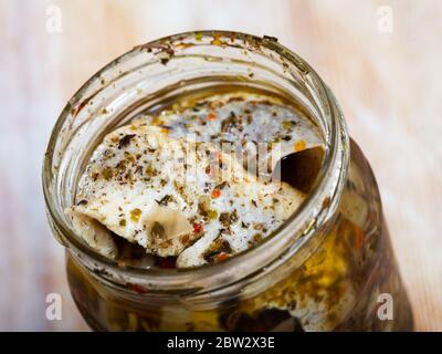 Primo piano di filetti di aringhe sottaceto piccante in olio in vaso di vetro aperto su fondo di legno Foto Stock