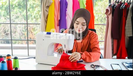 Piccola impresa di designer di moda donna musulmana Che Lavora e utilizza smartphone e tablet Con abiti al negozio di abbigliamento Foto Stock