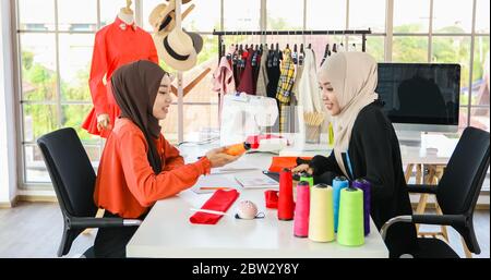 Piccola impresa di designer di moda donna musulmana Che Lavora e utilizza smartphone e tablet Con abiti al negozio di abbigliamento Foto Stock
