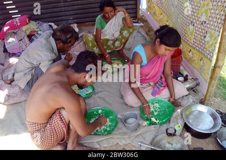 Nagaon, Assam / India - 29 2020 maggio: Abitanti del villaggio mangiare cibo sotto capannone temporaneo costruito su altopiano come le loro case sono sotto l'acqua in alluvione colpito Tetelisara villaggio vicino Kampur nel distretto di Nagaon di Assam il Venerdì. Foto Stock