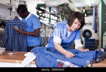 Focalizzato donna che lavorano nella moderna lavanderia, controllo qualità dei panni di pulizia Foto Stock