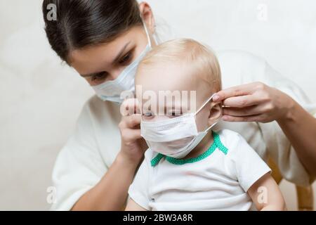 mamma mette su una maschera medica viso alla sua figlia piccola Foto Stock