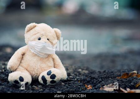 un orsacchiotto in una maschera medica si siede su asfalto sporco, spazio di copia Foto Stock