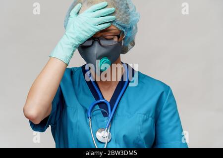 medico femminile con stetoscopio che indossa maschera protettiva e guanti in lattice su sfondo grigio chiaro Foto Stock