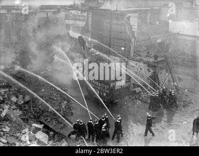 Un incendio feroce all'edificio demolito in Tottenham Court Road , Londra . I vigili del fuoco addestrano i loro tubi flessibili sui detriti . 12 gennaio 1935 Foto Stock