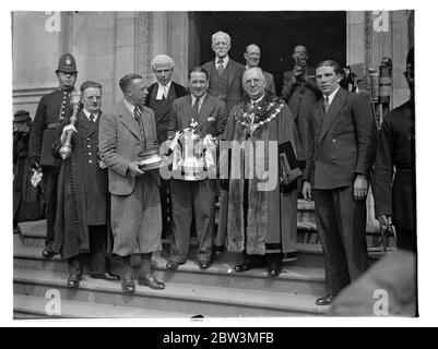 Il team Arsenal ha ricevuto un ricevimento civico a Islington . Guidare attraverso strade affollate . La squadra dell'Arsenal , vincitrice della Coppa d'Inglese , che portava la F A Cup , ha guidato attraverso grandi folle al Municipio di Islington , dove è stata loro data un'accoglienza civica . Il team è stato ricevuto dal Sindaco , Consigliere H G Coleman , che è stato un vecchio calciatore , nel municipio . Spettacoli fotografici , Alex James , il capitano dell'Arsenale che mostra la coppa alla folla . Nella foto è anche il Sindaco di Islington , consigliere H G Coleman . 28 aprile 1936 Foto Stock