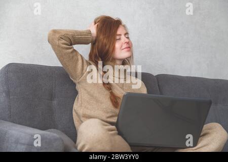 La giovane donna si allunga dopo aver finito il lavoro o la conferenza online sul divano. Freelance, che lavora a casa Foto Stock