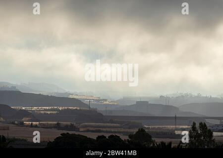 Buio e moody alba luce del sole nelle nuvole delle montagne che illuminano le piantagioni di banane sopra la costa occidentale di Tenerife, Canary Isla Foto Stock