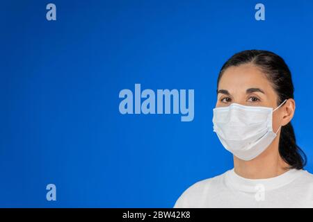 Donna isolata con maschera protettiva su sfondo blu e con ampio spazio per la copia. Concetto di problema di salute, misura preventiva contro Covid-19 Foto Stock