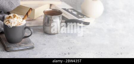 Tazza di cioccolata calda con crema di latte e cannella su tavolo bianco in cemento con libro. Inverno relax umore e higge sfondo. Immagine grande per banner Foto Stock