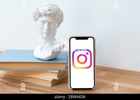 Kiev, Ucraina - 28 maggio 2020: Logo Instagram su iPhone X schermo su tavolo di legno con libri e David busto statua. Social network. Foto Stock