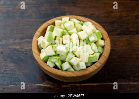 zucchine tagliate a dadini in una piastra di legno su fondo di legno marrone Foto Stock