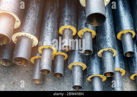 Mucchio di molti nuovi tubi in acciaio isolati neri nel cantiere municipale all'aperto. Rinnovo o ricostruzione di condutture principali di riscaldamento. Città Foto Stock