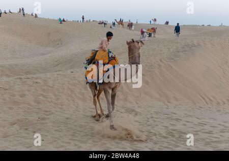 Un cammelliere (autista del cammello) che porta il cammello decorato mentre parla sui loro cellulari sulle dune di sabbia di sam del deserto di Thar con i turisti durante il tramonto Foto Stock