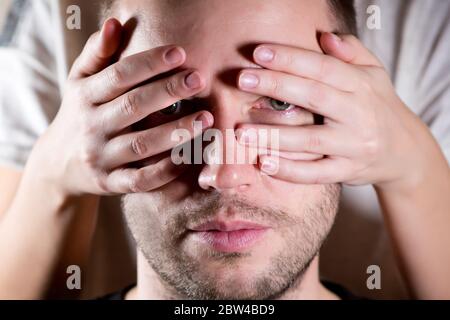 un uomo guarda attraverso le dita di una donna che copre il viso con le mani. primo piano Foto Stock