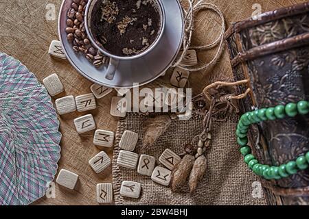 Concetto isoterico di divinazione e predizione. Carte Tarocchi, rune, caffè in una tazza, rosario su un tavolo sullo sfondo di un vecchio petto Foto Stock