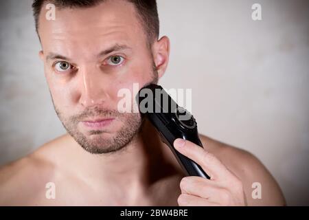 un giovane che sta per radere la barba corta con un rifinitore Foto Stock