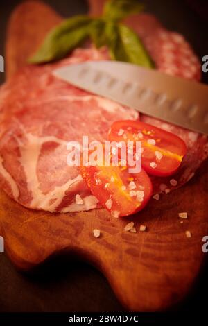 Antipasti di salame e pomodori prugnosi freschi con sale di roccia su tavola di legno. Foto Stock