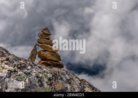 Una pila di pietra, si trova sulla cima di una montagna, a Whistler, Canada, che si affaccia su un paesaggio nuvoloso. Foto Stock