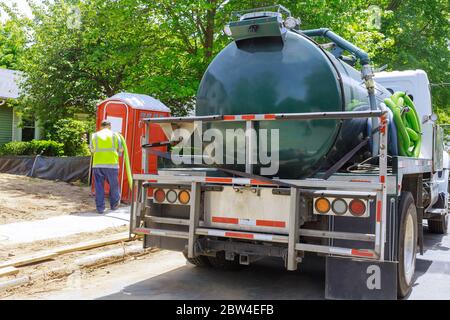 Camion fognario su lavoratore che pompano feci fuori del gabinetto a noleggio per lo smaltimento e la pulizia in costruzione Foto Stock