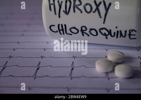 Effetti avversi sul cuore da parte di idrossiclorochina o clorochina. Pillole su un elettrocardiogramma. Contenitore bianco con scritta 'idrossiclorochina' Foto Stock