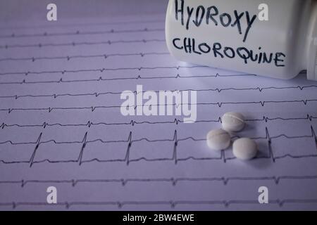 Effetti avversi sul cuore da parte di idrossiclorochina o clorochina. Pillole su un elettrocardiogramma. Contenitore bianco con scritta 'idrossiclorochina' Foto Stock