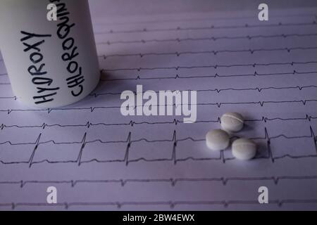 Effetti avversi sul cuore da parte di idrossiclorochina o clorochina. Pillole su un elettrocardiogramma. Contenitore bianco con scritta 'idrossiclorochina' Foto Stock