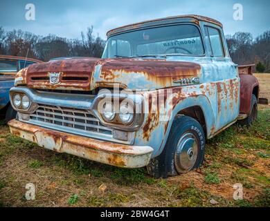 Un camion di pick-up Ford F100 antico parcheggiato in un campo agricolo lungo la strada blu con patina arrugginita ancora in buona forma Foto Stock