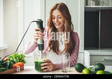 Donna caucasica con capelli rossi e fracelle che fanno il succo di verdure spremendo avocado e carote Foto Stock