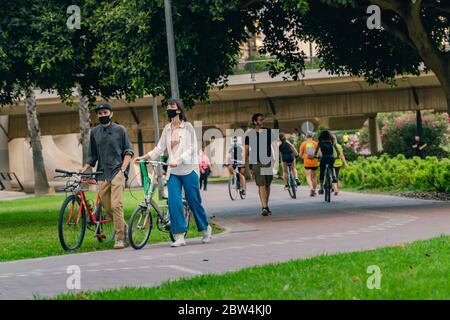 Valencia, Spagna - 28 maggio 2020: Giovane coppia con maschere nere di protezione del viso che cammina con le loro biciclette al parco. Nuovo normale durante COVID-19, cor Foto Stock