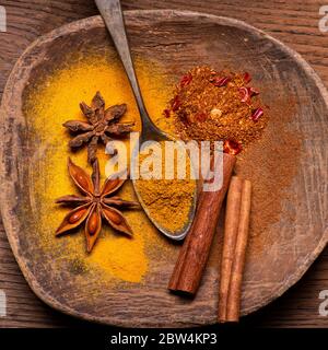 in una ciotola rustica in legno, in primo piano, alcune stelle di anice stellato, bastoncini di cannella e alcune spezie in polvere Foto Stock