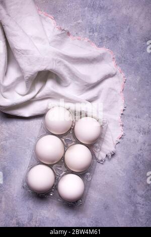 sullo sfondo grigio, con vista dall'alto, un tovagliolo di cotone e mezza dozzina di uova bianche per la preparazione di ricette culinarie Foto Stock