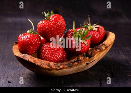 in primo piano, una ciotola di legno con fragole mature su rustico sfondo di legno Foto Stock