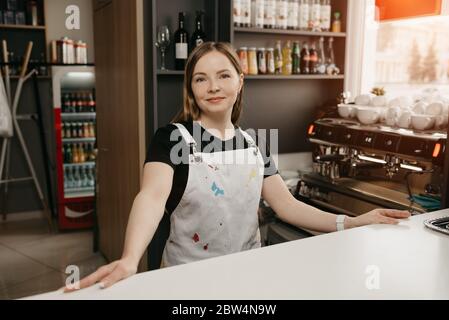Una barista femminile con un grembiule bianco si pone dietro il bar in un  caffè. Una bella donna imprenditore nel suo bar Foto stock - Alamy
