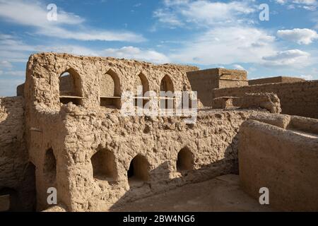 Luce del sole calda su rovina nel centro storico di Harat al Bilad di Manah, Oman sotto il cielo blu nuvoloso Foto Stock