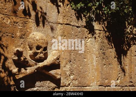 Teschio cupo con le ossa trasversali scolpite in una parete di pietra sulla strada di San Giacomo, sulla strada che conduce a Santiago de Compostela in Spagna. Foto Stock