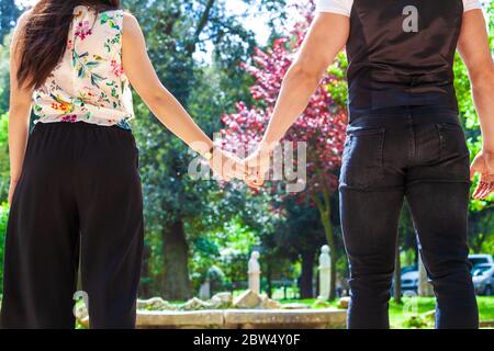 Coppia impegnata amorevole che cammina mano in mano, visto dalla parte posteriore con un tiro stretto. Due persone, uomo e donna, tengono le mani all'aperto. Foto Stock