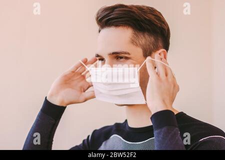 Ritratto di un giovane sportivo sicuro che ascolta musica negli auricolari wireless e indossando una maschera medica. Uomo sportivo felice che indossa una maschera protettiva Foto Stock