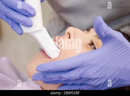 Dentista irriconoscibile in guanti di lattice utilizzando uno strumento professionale per esaminare i denti della giovane donna durante il lavoro in clinica moderna Foto Stock