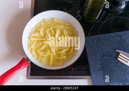 Patate sbucciate e tagliate che vengono fritte in una padella con olio. Foto Stock