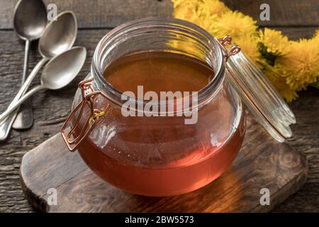 Un vaso di miele di dente di leone con fiori freschi sullo sfondo Foto Stock