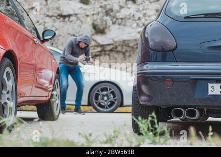 Vista posteriore di un'auto blu modificato con due scarichi, l'uomo in lontananza sfocato indossando una felpa con cappuccio accovacciato tenendo uno smartphone e scattando una foto di Foto Stock