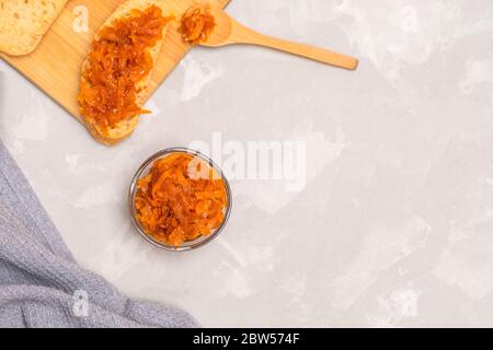 Marmellata di carote fatte in casa in una ciotola con toast e cucchiaio di legno su tavolo da cucina in cemento grigio. Immagine con spazio di copia, vista dall'alto Foto Stock