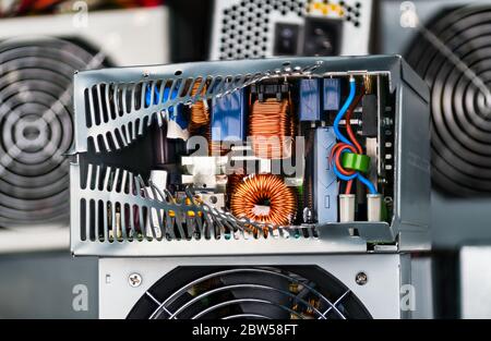 Smaltimento dei rifiuti elettronici. Componenti elettronici all'interno della scatola dell'unità di alimentazione danneggiata. Induttori toroidali con avvolgimento del filo di rame, condensatori e bobina. Foto Stock