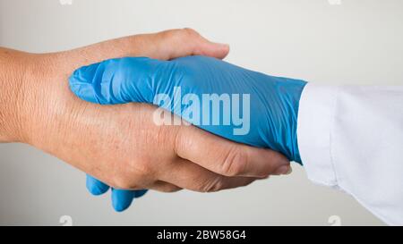 Scuotere le mani dell'operatore sanitario con un paziente malato durante la pandemia COVID-19. Guanti protettivi blu e non protetti. Aiuto simbolico o t Foto Stock