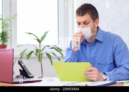 il lavoratore malato in maschera medica si siede alla scrivania Foto Stock