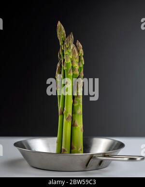 foto concettuale, un mazzo di asparagi enormi si trova al centro di una piccola teglia in acciaio su sfondo bianco e nero. Foto Stock