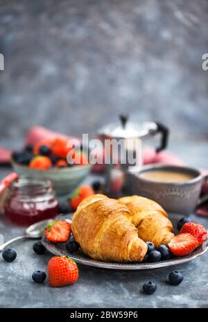Colazione continentale con croissant, frutti di bosco freschi, caffè e marmellata, sfondo grigio Foto Stock